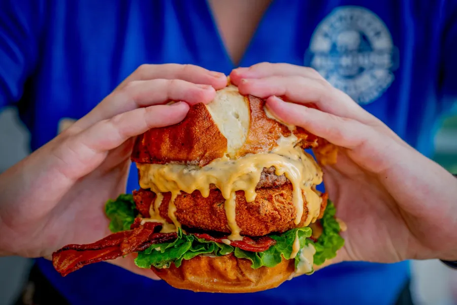A server holding a bacon cheeseburger on a pretzel bun
